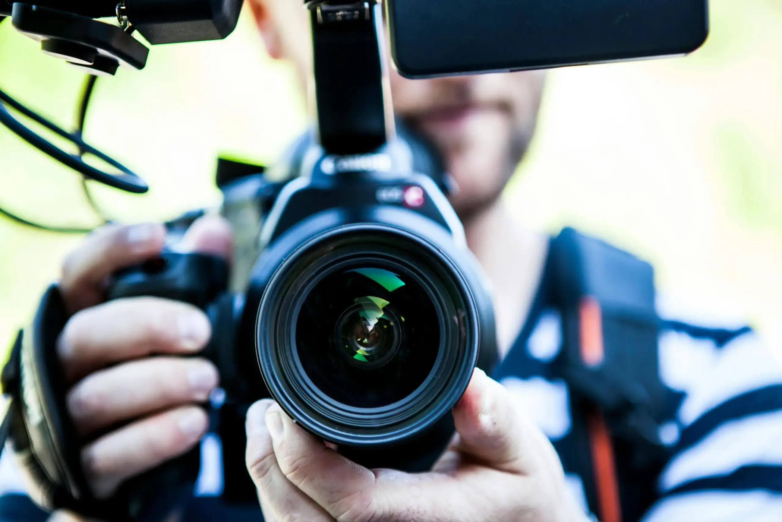 Un vidéaste tenant une caméra professionnelle avec un écran et un micro, en train de filmer en extérieur.